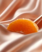 Fresh mandarin orange segment on smooth silky fabric with soft pink folds creating elegant contrast between textures and colors.