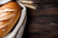 Fresh baked crusty bread loaf wrapped in linen cloth with wheat ears on dark wooden background, rustic food photography with copy space for text.