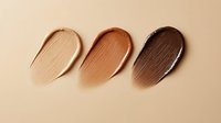 Makeup foundation swatches in different skin tones from light to dark on beige background. Cosmetic texture smears showing product consistency and coverage.