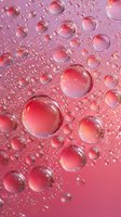 Transparent water droplets and bubbles on pink surface creating abstract macro texture with light reflections.
