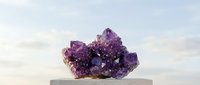 Purple amethyst crystal cluster on wooden platform against soft cloudy sky background for meditation and healing practices.