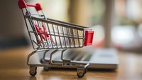 Empty miniature shopping cart on wooden surface with blurred background, representing retail, commerce and consumer behavior concepts.