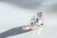 Sparkling crystal diamond casting rainbow light reflections and long shadow on white surface against soft gray background, luxury jewelry concept.