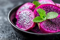 Fresh dragon fruit slices in vibrant magenta color garnished with mint leaves in dark ceramic bowl on textured black background, macro food photography.