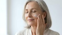 Mature Caucasian woman applying anti-aging face cream with gentle massage motions. Skincare routine for healthy glowing skin and wrinkle prevention.