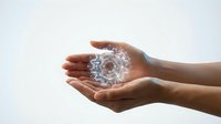 Hands holding transparent crystal sphere with water droplets on white background, isolated for design use.