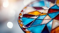 Colorful stained glass mosaic pattern in turquoise blue, amber and purple creates geometric triangular shapes with soft bokeh light effect in background.