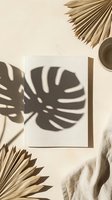 Blank white notebook with monstera leaf shadow on beige background, dried palm fans and linen fabric, minimal tropical flat lay mockup.