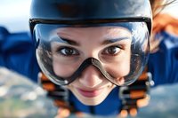 Close up portrait of young Caucasian woman wearing protective goggles and helmet while skydiving, expressing excitement and joy against blue sky background.