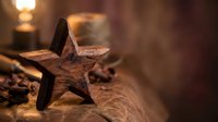 Rustic wooden star decoration on burlap fabric with warm candlelight creating cozy holiday atmosphere for seasonal home decor and festive celebrations.