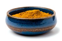 Ground turmeric powder in rustic blue ceramic bowl against white background, traditional Asian spice and superfood ingredient for cooking and wellness.