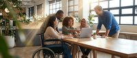 Diverse business team collaborating in modern office with wheelchair accessibility, promoting inclusive workplace culture and teamwork.