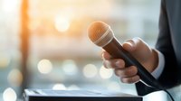 Professional speaker holding microphone against blurred background with warm sunlight, business presentation or public speaking concept for corporate events.