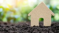 Small cardboard house silhouette planted in soil against green natural background, representing growth, eco living, and sustainable real estate concept.