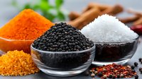 Colorful spices and seasonings in glass bowls - black caviar, sea salt, turmeric powder, cinnamon sticks and pink peppercorns on dark background for gourmet cooking.