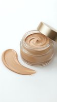 Luxury foundation cream in glass jar with golden cap and makeup swatch on white background for cosmetic advertising and beauty product marketing.