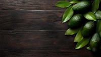 Fresh green avocados with glossy leaves arranged in corner on dark wooden background, creating dramatic lighting and negative space for text placement.