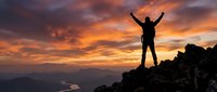 Silhouette of triumphant hiker with raised arms celebrating success on mountain peak against dramatic orange sunset sky. Achievement and adventure concept.