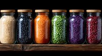 Glass jars filled with colorful dried legumes and grains on wooden shelf against black background, arranged in rainbow sequence for kitchen storage and decoration.