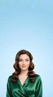 Young woman with long, voluminous wavy brown hair and fair complexion wearing emerald green satin wrap top against soft blue background. Suitable for business, fashion, and lifestyle marketing.