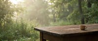 Rustic wooden table with coffee cup in serene forest setting, morning sunlight filtering through trees, peaceful outdoor retreat for relaxation and contemplation.