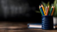 Colorful wooden pencils in dark blue textured holder on wooden desk with blurred background, minimalist workspace setup for creative design and art projects.