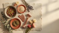 Flat lay arrangement of dried herbs, grains, and flowers on neutral linen with ceramic bowls, featuring lavender and botanicals for wellness, cooking, and natural product styling.