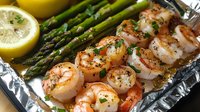 Grilled jumbo shrimp with fresh asparagus spears and lemon slices on aluminum foil, seasoned with herbs and spices, glistening with butter sauce.