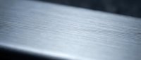 Brushed metal surface with fine linear texture and reflective finish for industrial design backgrounds and modern technology applications.