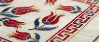 Traditional embroidered textile with red and blue floral motifs on cream fabric featuring decorative border pattern for cultural crafts and heritage design projects.