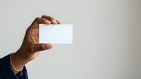 Close-up of male hand holding blank white business card against neutral background, suitable for corporate branding and identity mockups.