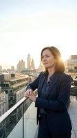 Middle-aged Caucasian businesswoman in navy blazer standing on rooftop terrace overlooking urban skyline at golden hour. Professional corporate portrait for business, leadership, and success themes.