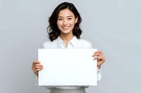 Young Asian businesswoman holding blank white paper sign with confident smile for marketing presentations and promotional campaigns.