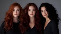 Three diverse women with long wavy hair in black outfits posing together against gray background for beauty and fashion photography concepts.