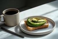 Fresh sliced avocado on toasted bread with black sesame seeds served on ceramic plate next to cup of black coffee in morning sunlight with shadows.