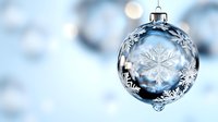 Transparent glass Christmas ball ornament with delicate white snowflake pattern against soft blue bokeh background creates magical winter holiday atmosphere.