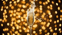Champagne glass with splash against golden bokeh lights, perfect for celebration, New Year, wedding, and festive event marketing materials.