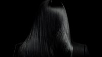 Sleek, straight black hair from behind against dark background, showcasing smooth texture and shine for luxury haircare advertising.