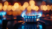 Blue flame on gas stove burner with warm bokeh lights in background, close up view showing kitchen appliance detail in dark ambient setting.