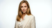 Professional blonde businesswoman in beige suit jacket smiling confidently against white background for corporate marketing materials.