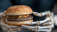 Spooky skeleton hands holding juicy cheeseburger with beef patty and melted cheese on sesame bun against dark background, creative Halloween food photography.