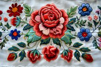 Traditional floral embroidery pattern with large coral rose as centerpiece, surrounded by blue wildflowers and green foliage on white fabric background.