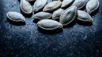 Raw sunflower seeds scattered on dark slate surface for healthy snacking and cooking ingredients in rustic kitchen setting.