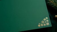 Flat lay composition featuring teal green paper with gold snowflake decorations and evergreen foliage, suitable for holiday greeting cards and seasonal marketing materials.
