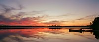 Serene lake at sunset with moored boat, calm water reflecting vibrant orange and pink sky, peaceful nature landscape for travel and relaxation content.