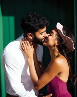 Young couple kissing outdoors against green wall background. Man with dark beard wearing white shirt and woman with long dark hair in burgundy dress embrace romantically in natural sunlight for relationship and love concepts.