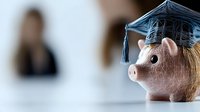 Pink ceramic piggy bank wearing graduation cap against blurred background, symbolizing education savings and financial planning for college studies.