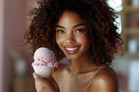 Young African American woman with curly hair smiling while holding pink ice cream cone in bright indoor setting for summer lifestyle content.