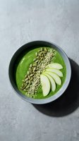 Green smoothie bowl topped with pumpkin seeds, quinoa, and sliced apple. Nutritious breakfast or healthy snack option for wellness and diet-conscious consumers.