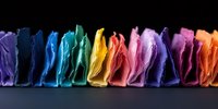 Vibrant rainbow colored fabric waves in motion against dark background, flowing silk material creates dramatic folds and textures in spectrum arrangement.
